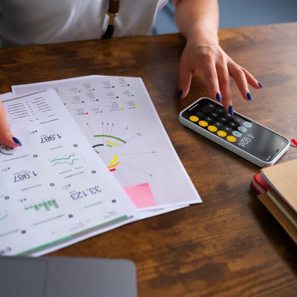 Une personne utilise une calculatrice et un téléphone sur une table, en lien avec une proposition de consommateur.