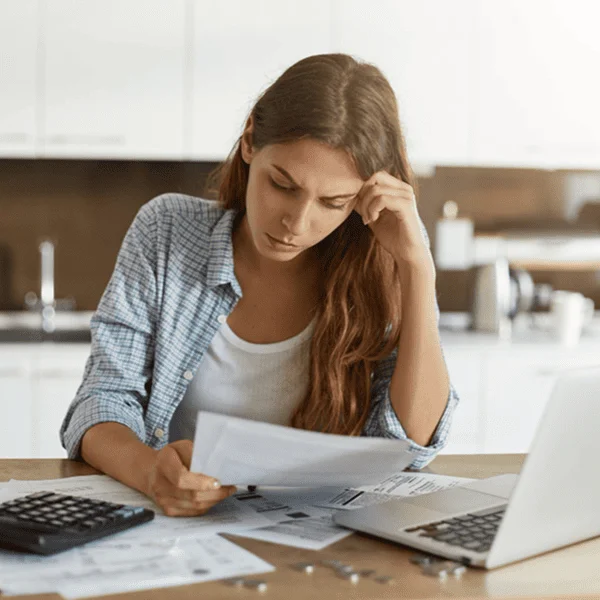 Femme utilisant un ordinateur portable avec des documents sur une table, concentrée sur son travail.