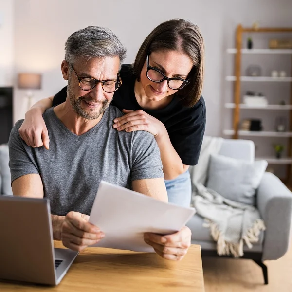 Homme et femme examinant des documents sur un ordinateur portable.