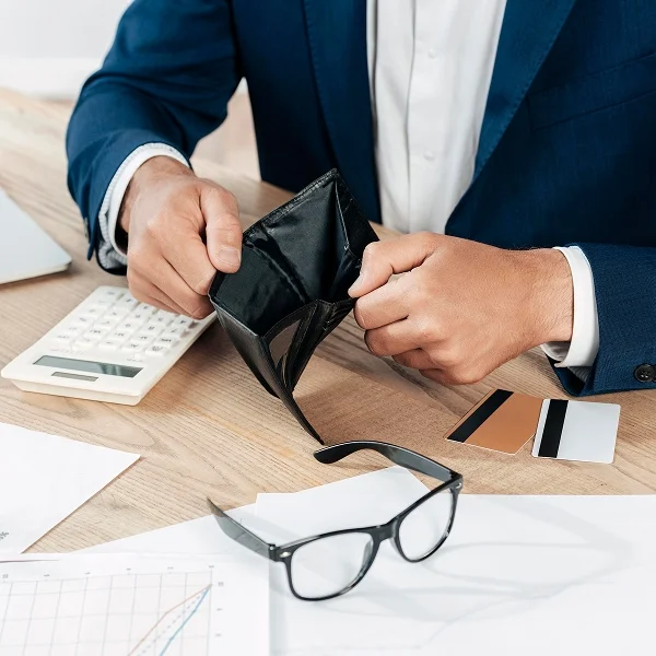 Un homme en costume tient un portefeuille vide, exprimant une préoccupation financière.