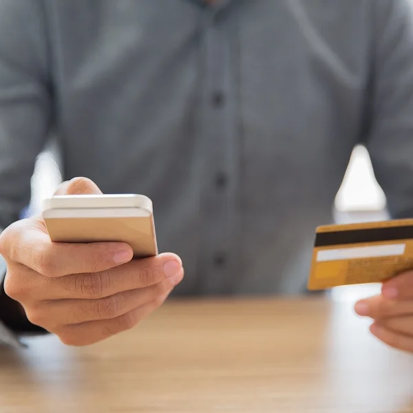 Homme tenant une carte de crédit et un téléphone mobile, prêt à effectuer un paiement.