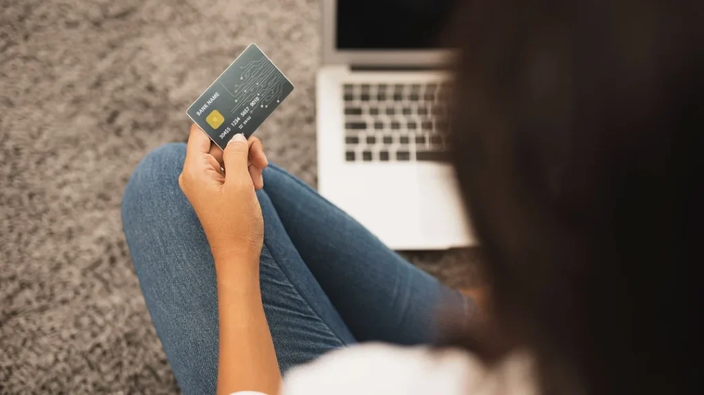 Une femme assise par terre tient une carte de crédit dans ses mains.