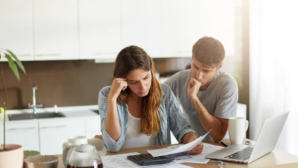 Un homme et une femme assis à une table, utilisant un ordinateur portable et entourés de documents.
