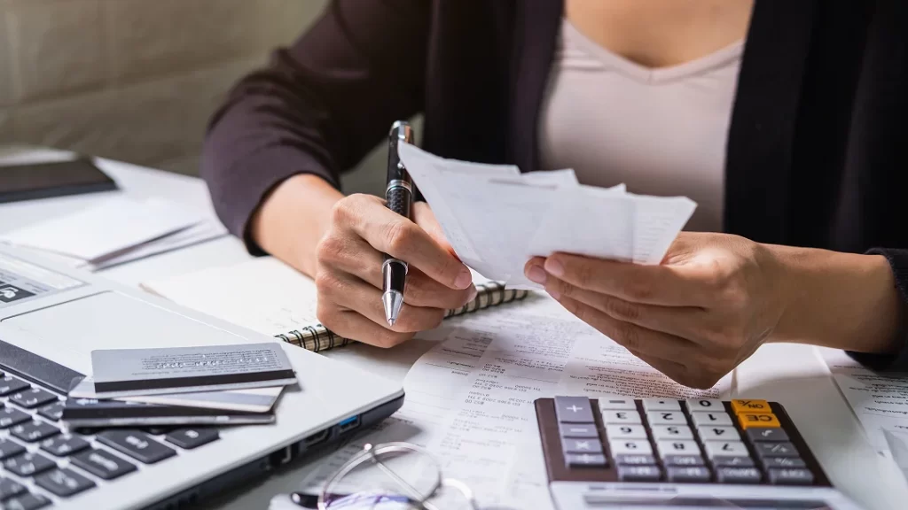 Femme d'affaires écrivant sur du papier avec un stylo, un calculateur à côté.