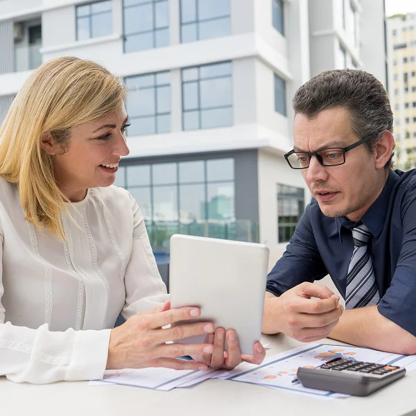 Un homme et une femme assis à une table, utilisant une tablette ensemble.