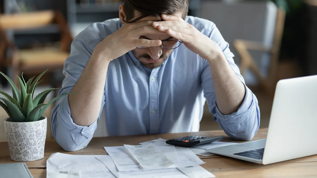 Un homme assis à un bureau, la tête dans les mains, semblant stressé ou accablé.