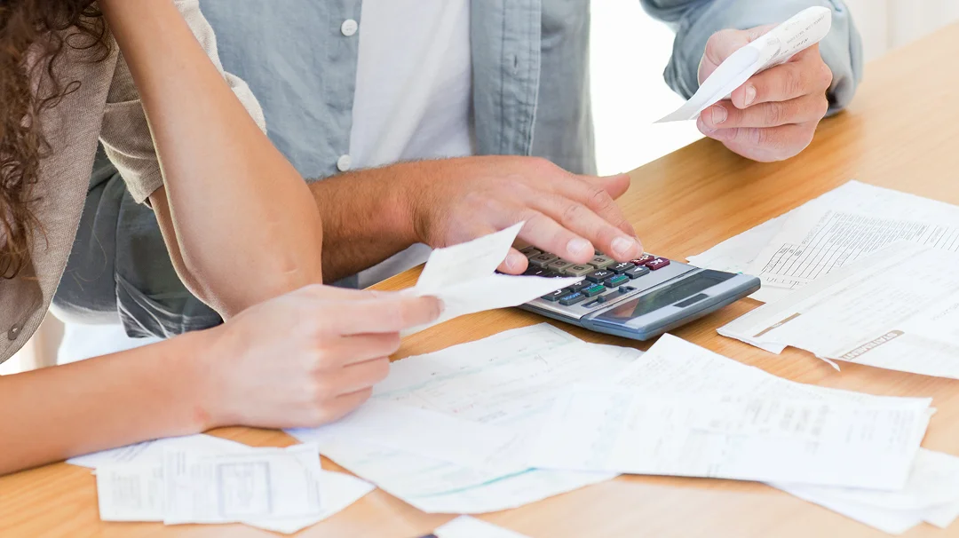 Un homme et une femme examinent un calculateur et des documents sur une table.