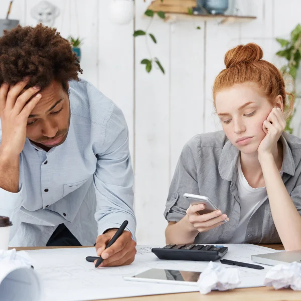 A man and woman sit at a table, reviewing papers and using a calculator to discuss personal debts.