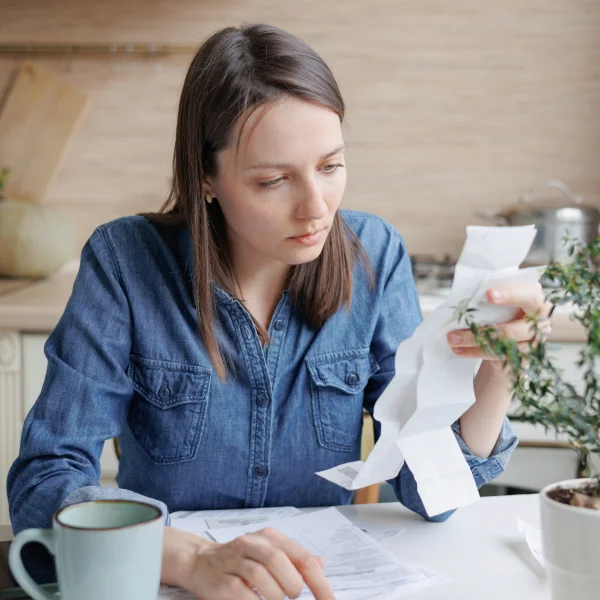 A woman reviews her bills while contemplating financial decisions, with a green plant in the background.