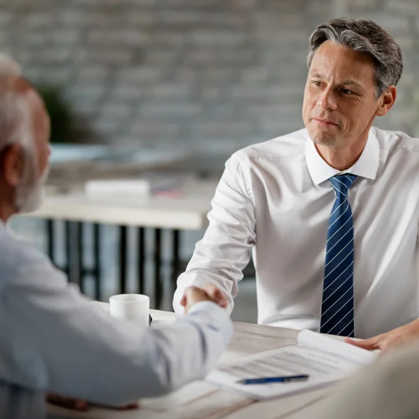Un homme en chemise blanche et cravate serre la main d'un autre homme, représentant un moment de collaboration professionnelle.