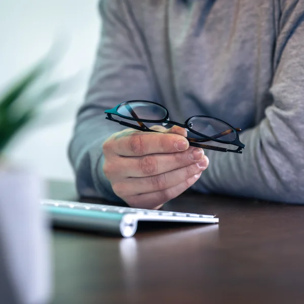 Un homme tient une paire de lunettes sur son bureau, avec un document intitulé "Proposition de consommateur" à côté.